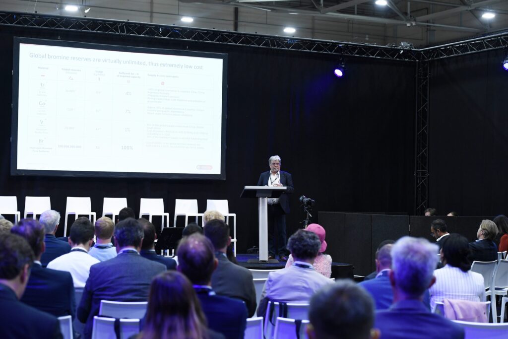 A speaker at the conference in front of a screen showing some of the attendees