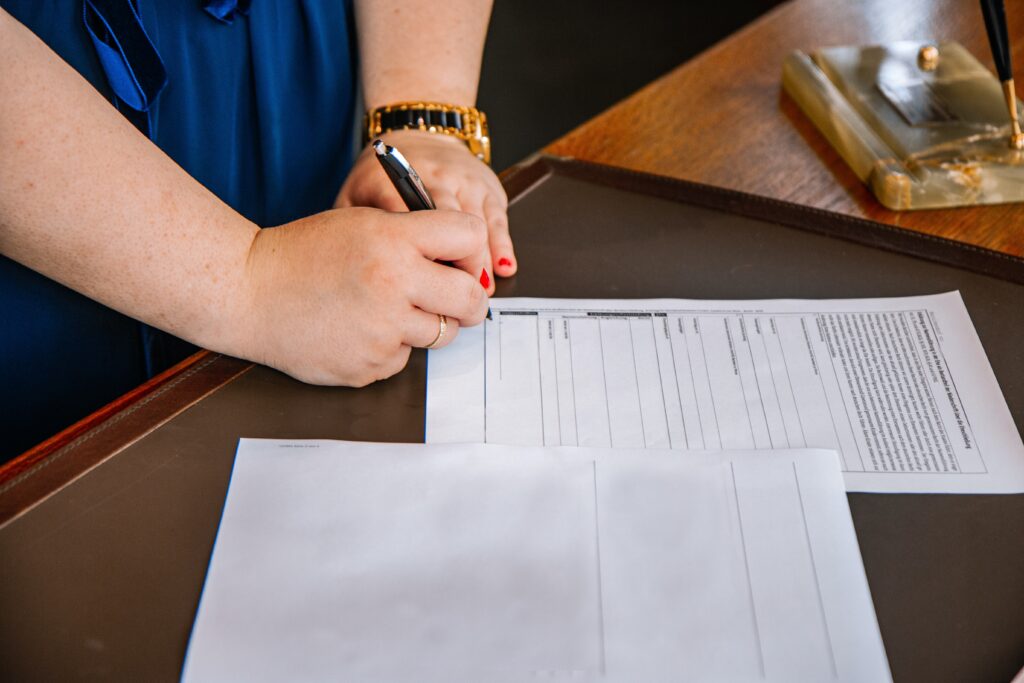 A woman fills in a form on paper with a black pen.