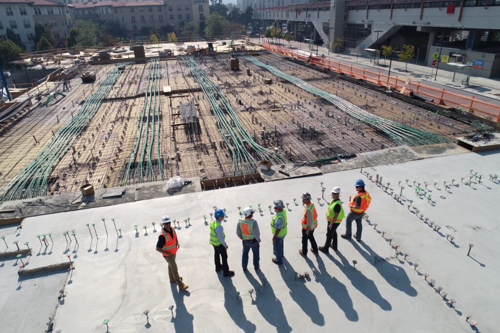 Birds eye view of seven construction site workers in hi-vis looking at a construction site ahead of them.