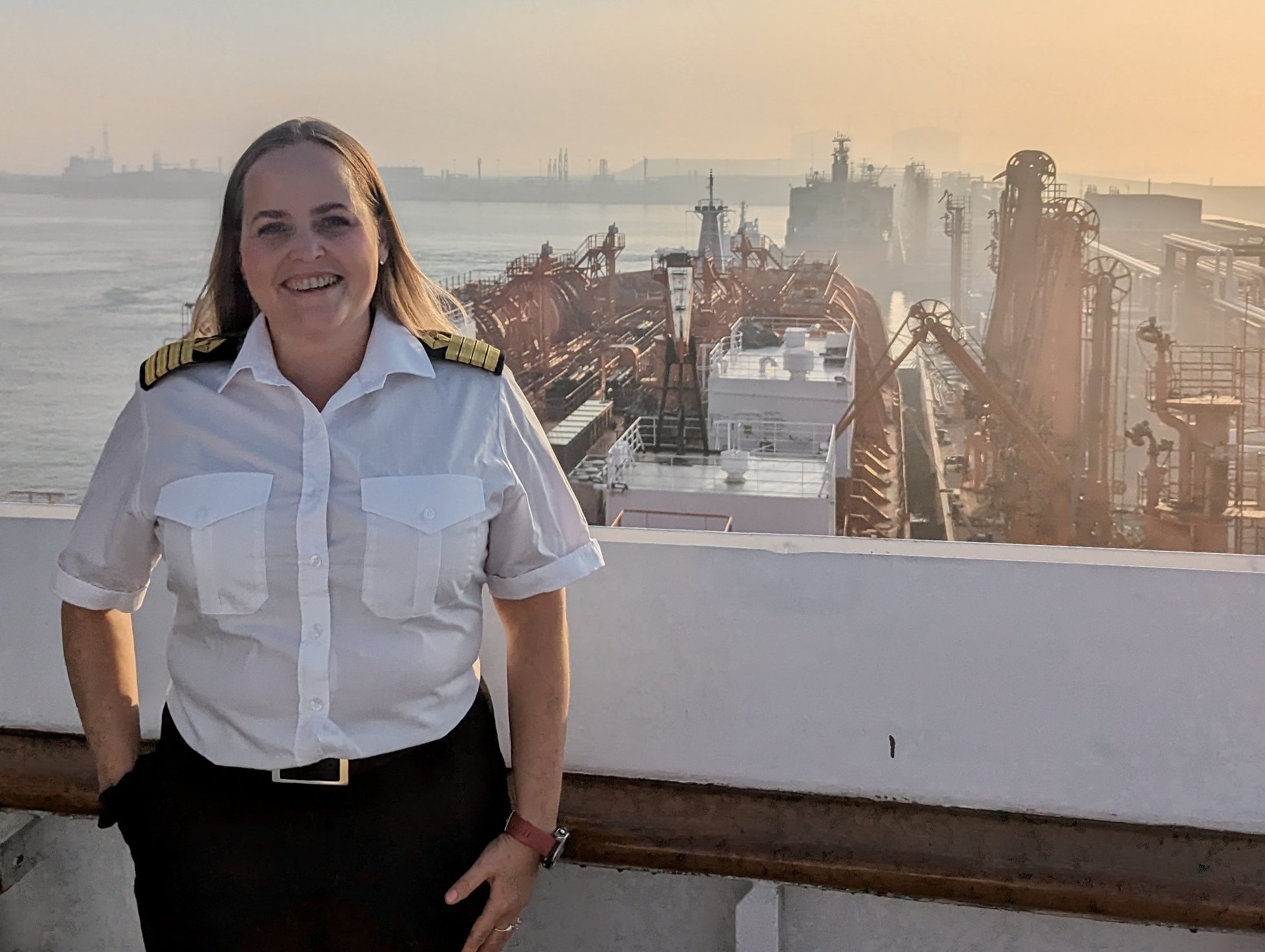 A woman in a captain's uniform smiling with a view of the port behind her