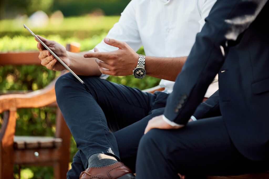 Two men on park bench looking at electronic tablet.