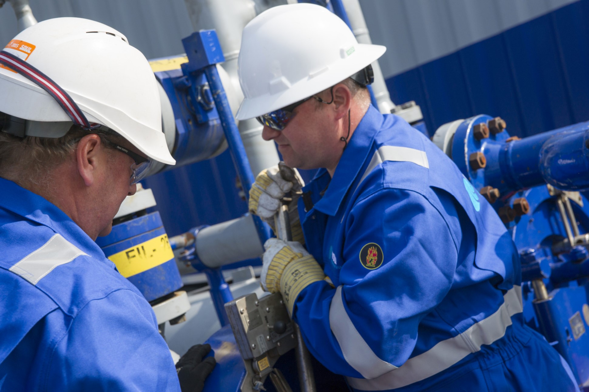 two men in hard hats and high vis looking at pipes