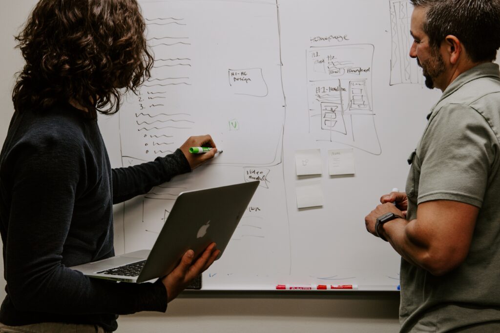 Man and a woman writing on a whiteboard, woman holds laptop