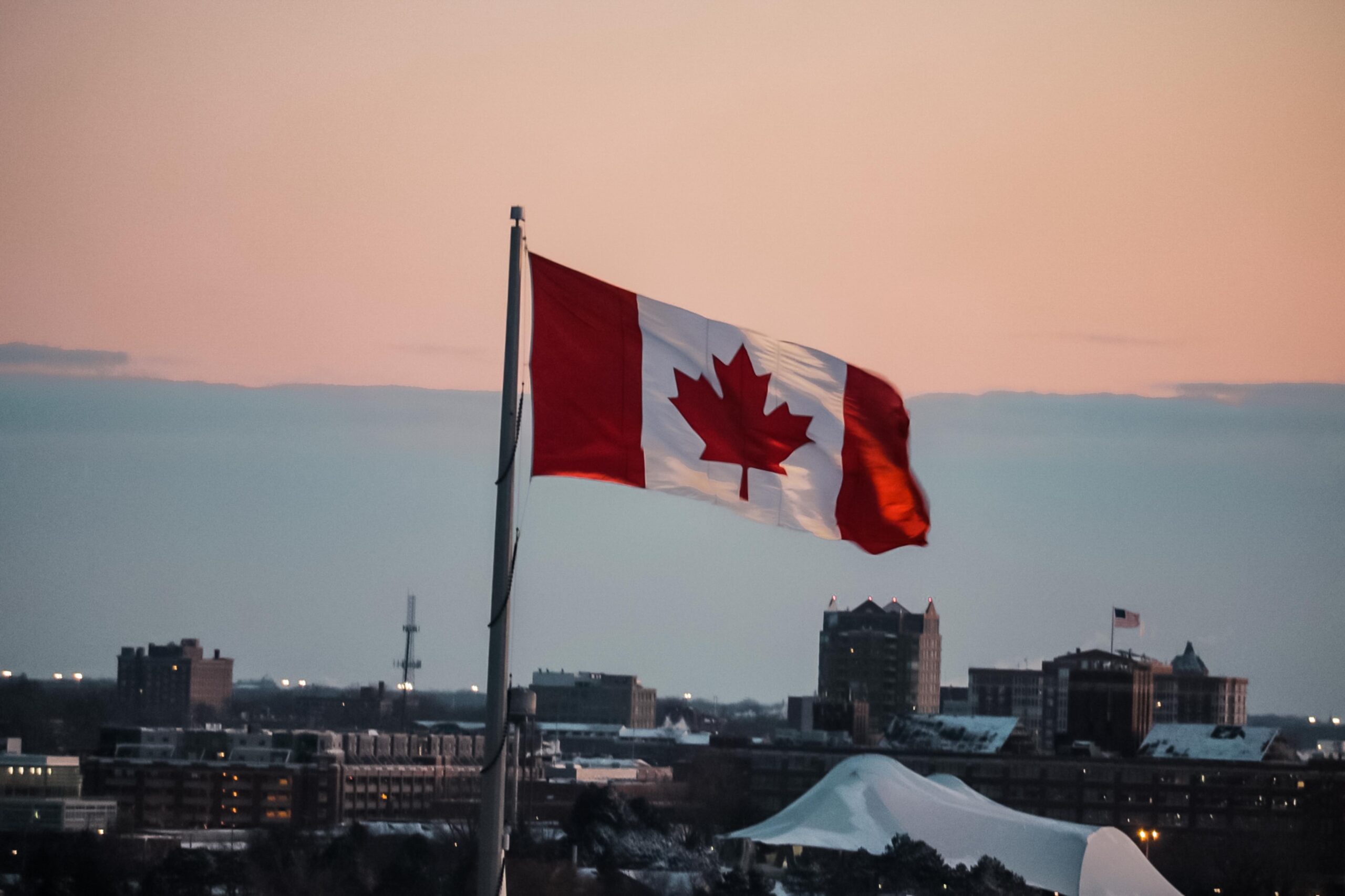 Canada flag on a pole in front of orange sky and city buildings
