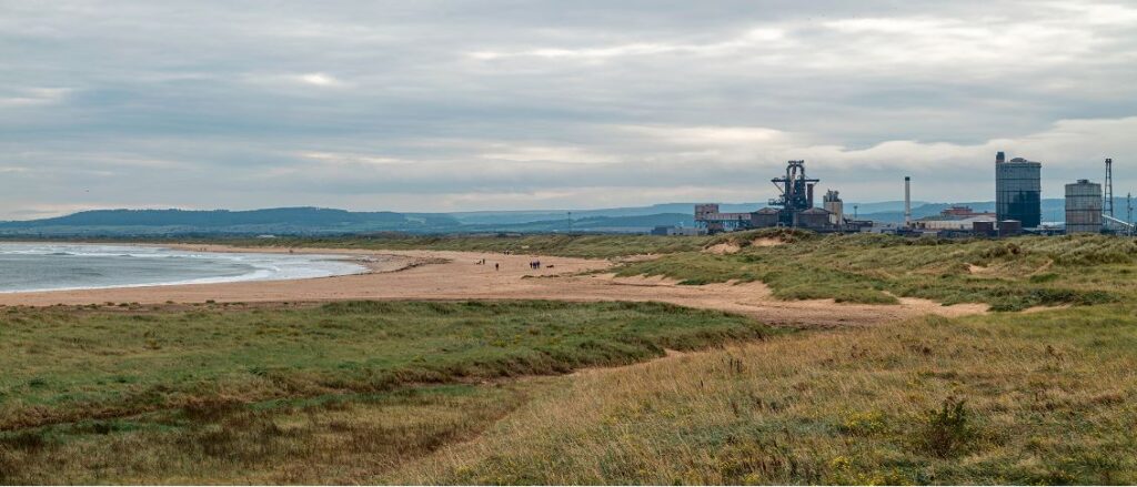 a beach with a factory and a body of water