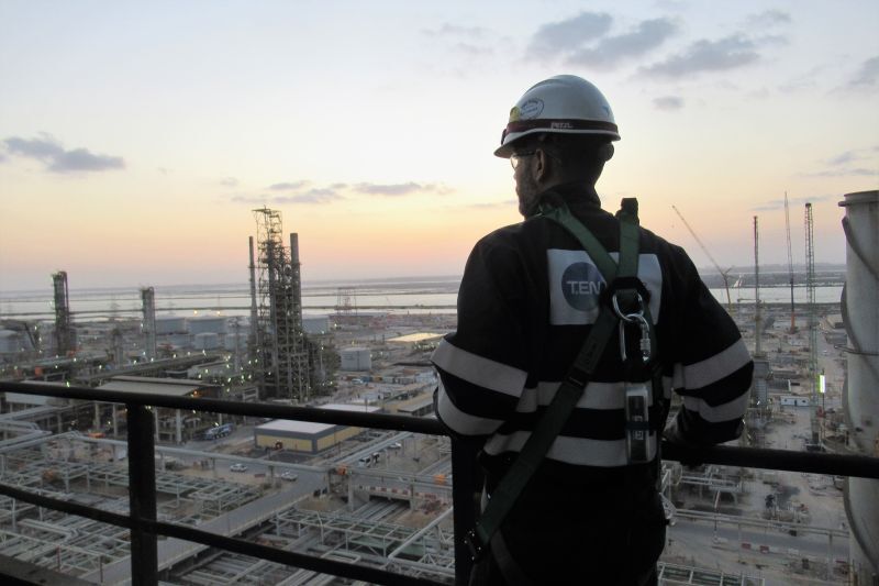 A man in high vis and hard hat with Technip Energies logo overlooking an industrial site at sunset