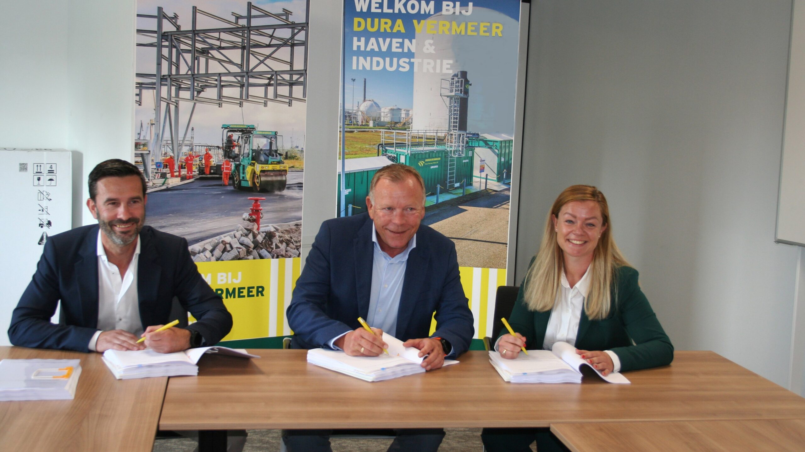 Two men and one woman sat at table, smiling and signing papers.